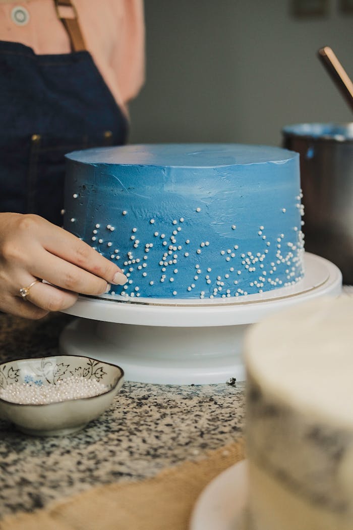 Close-up of a woman decorating a blue cake with white sprinkles.