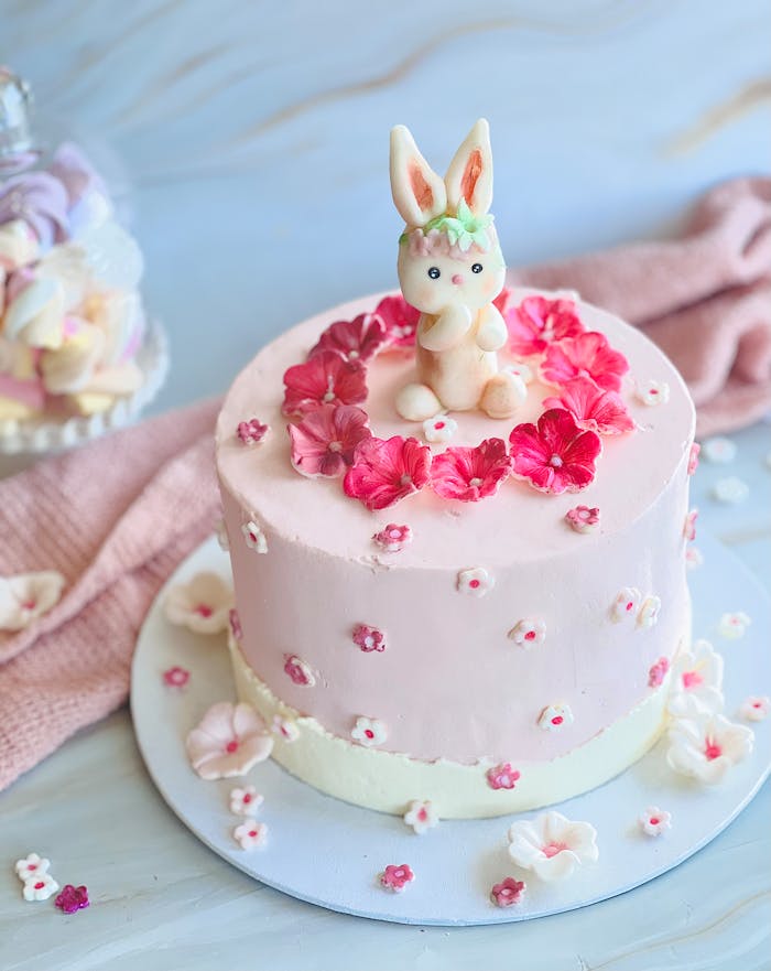 Charming pink cake adorned with a fondant bunny and vibrant floral decorations, perfect for celebrations.