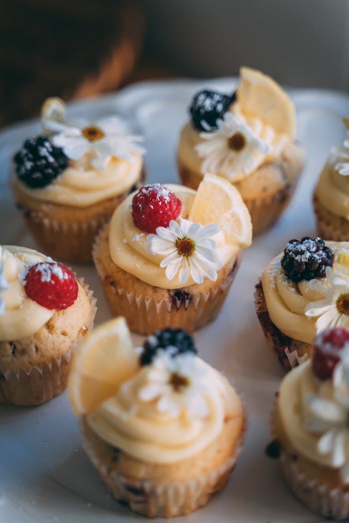 Assorted cupcakes with cream frosting, lemon slices, berries, and flower decorations.