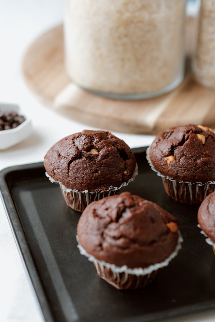 Freshly baked chocolate muffins with choco chips on a baking tray, perfect for a sweet treat.