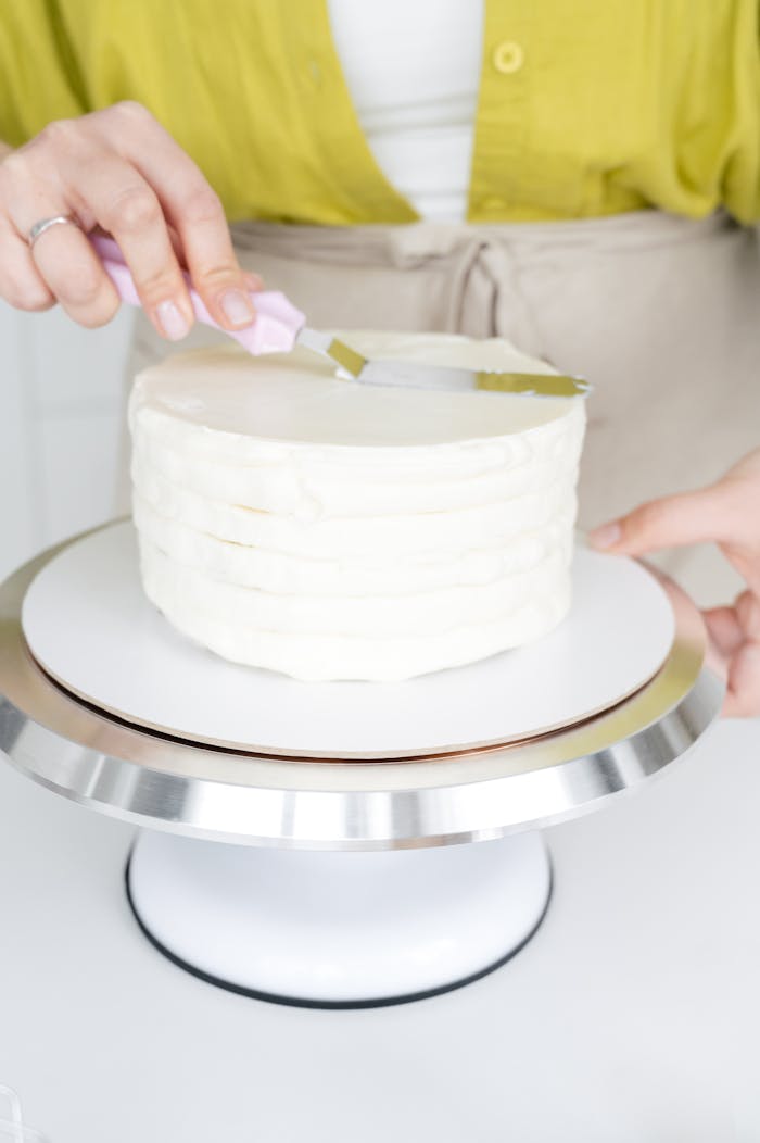 services-03 Woman wearing apron aligning cake with cream and cooking spatula on rotating stand